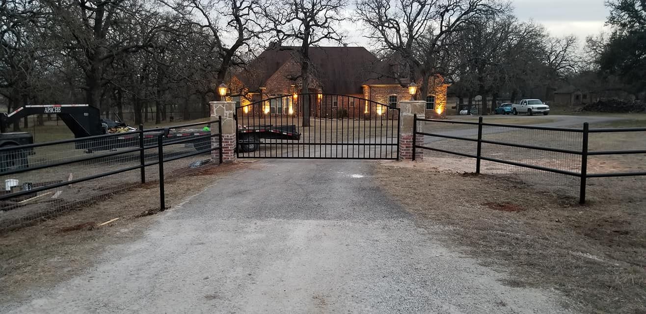 A driveway with a gate and a fence leading to a house.