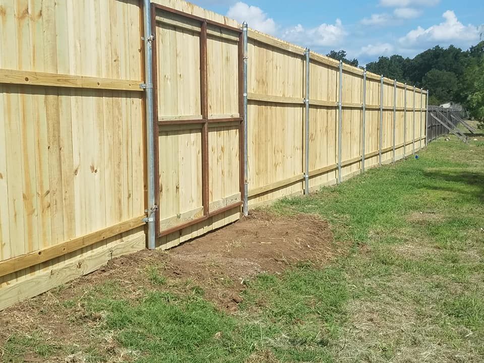 A wooden fence with a sliding gate in the middle of a grassy field.