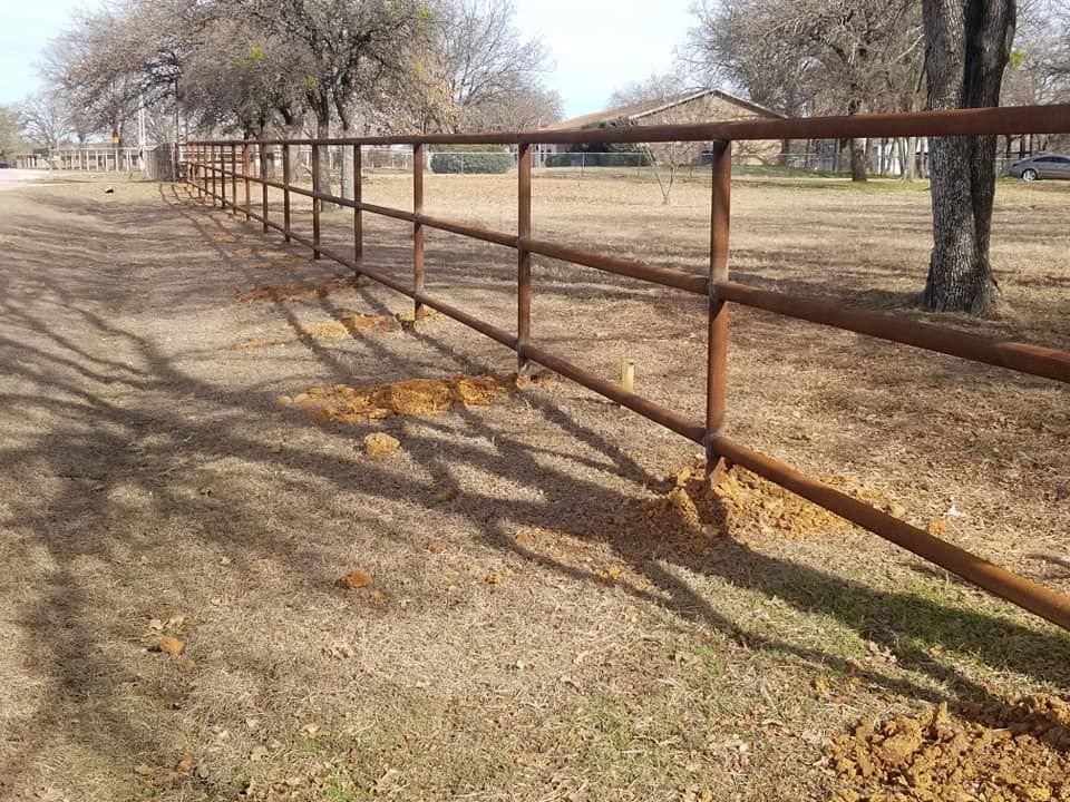 A rusty metal fence surrounds a dry grass field.