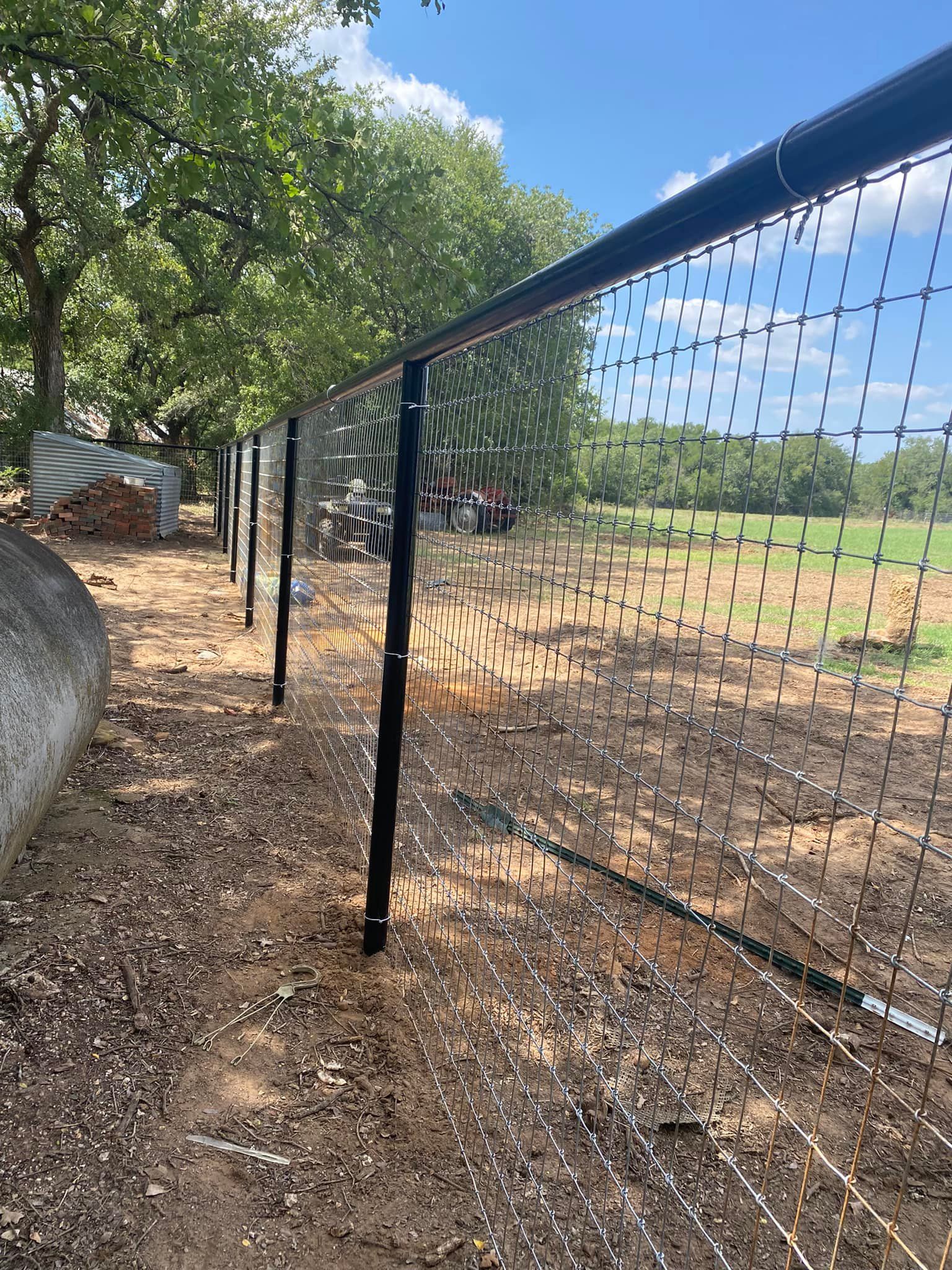 A fence is surrounding a field with trees in the background.