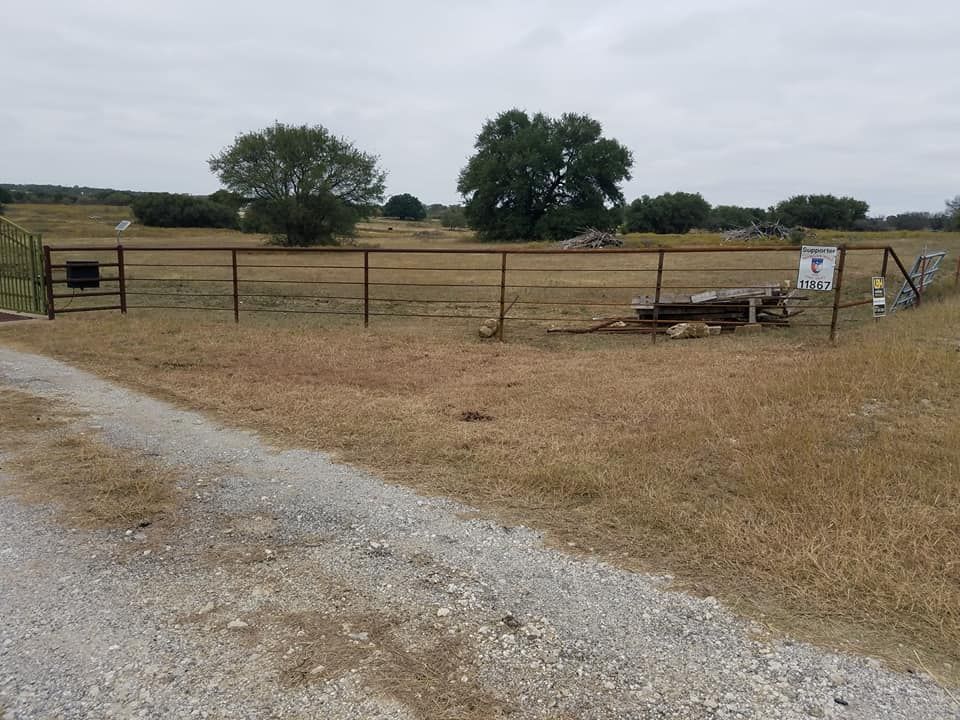 A dirt road leading to a fenced in field with trees in the background.