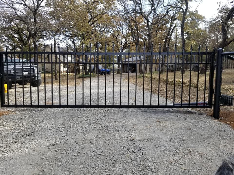 A black metal gate is open to a gravel driveway.