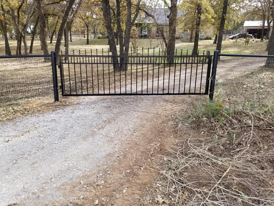 A black metal gate is sitting on the side of a dirt road.