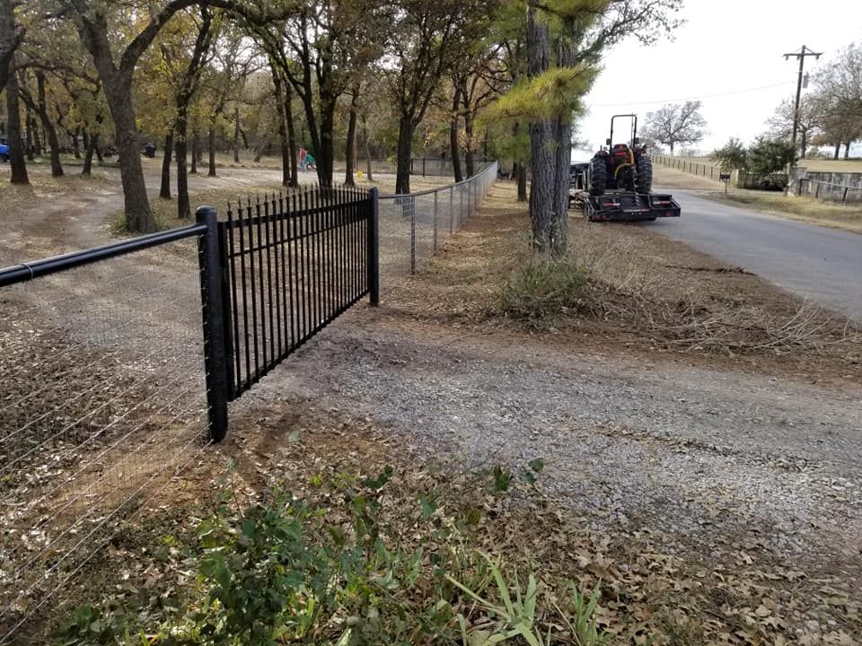 A black metal gate is sitting on the side of a dirt road.