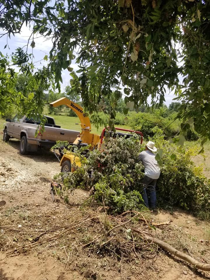 A man is standing next to a tree chipper in a field.