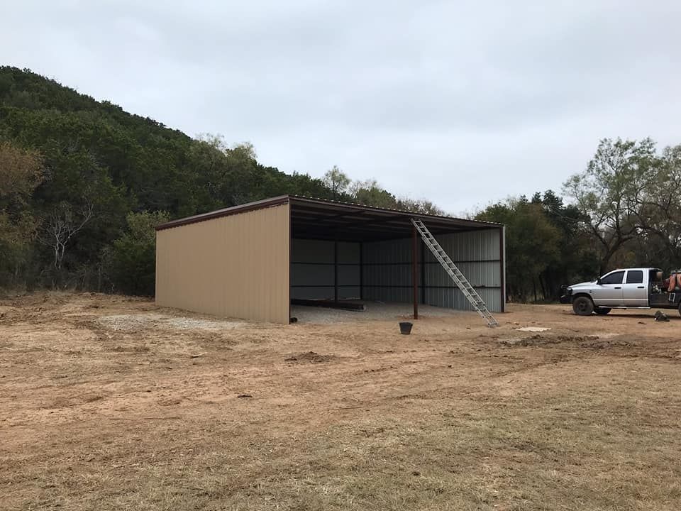A white truck is parked in front of a metal building in a field.