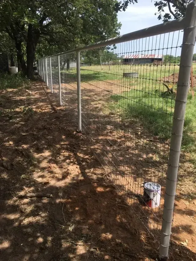 A fence with a bucket of paint on the ground next to it
