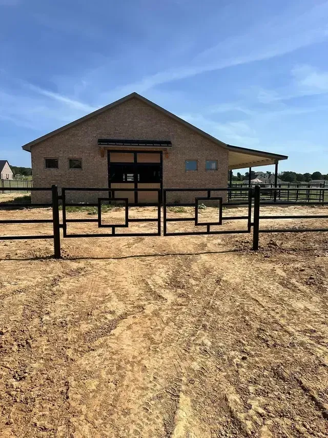 A horse stable with a fence and a barn in the background.