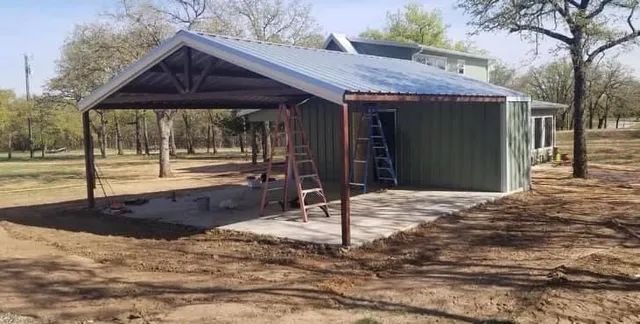A green house with a metal roof is being built in the middle of a field.