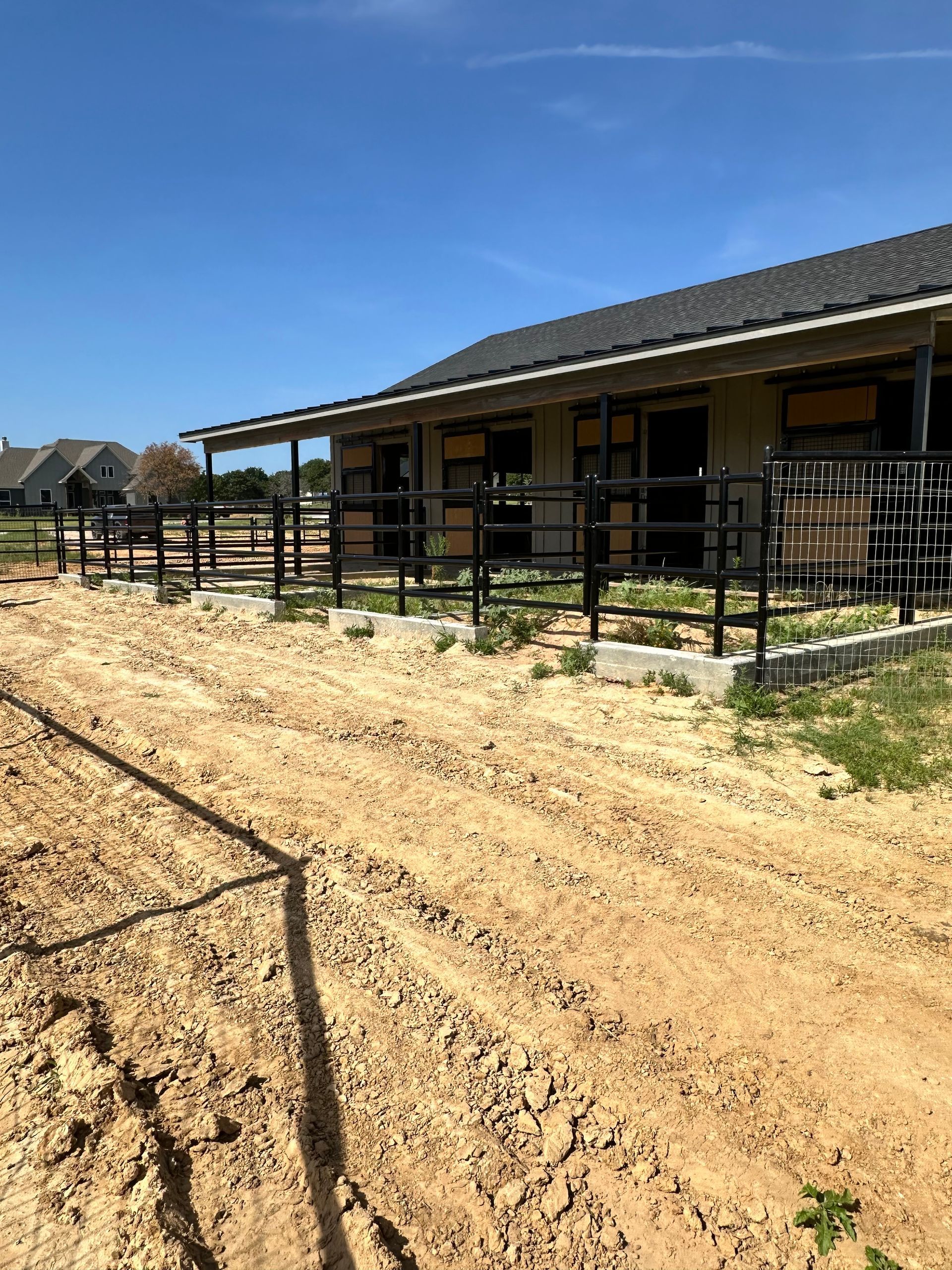 A dirt road leading to a horse stable with a house in the background.