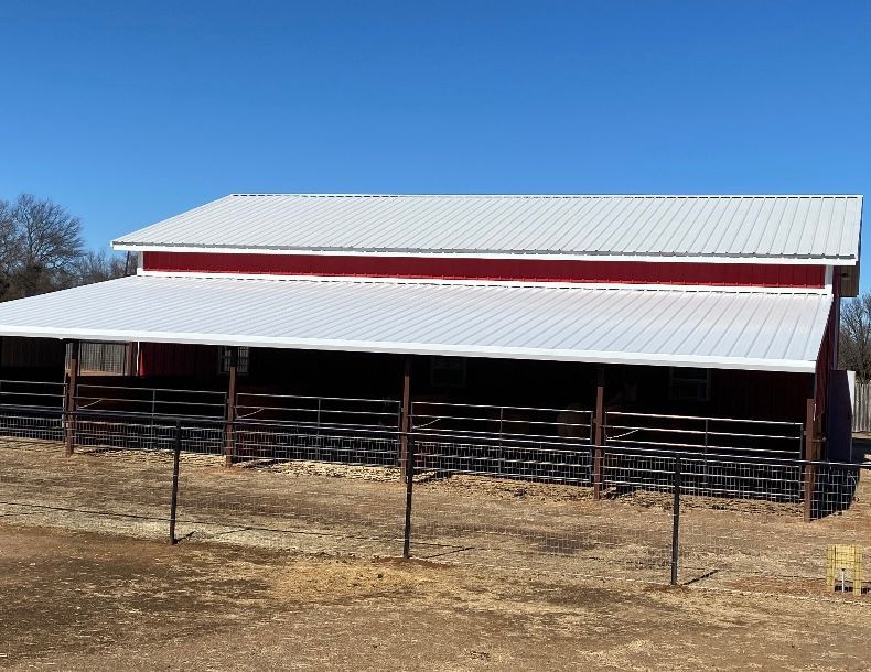 A red barn with a white roof and a fence in front of it.