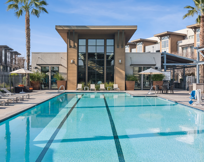 Modern apartment pool with clear blue water, lounge chairs, and palm trees in a sunny courtyard