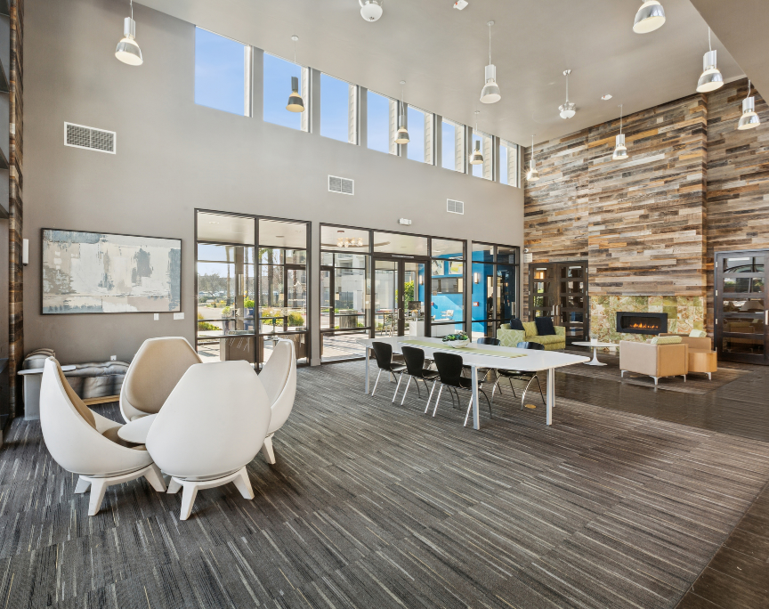 Modern lobby lounge with white chairs, tables, large windows, and a wood accent wall