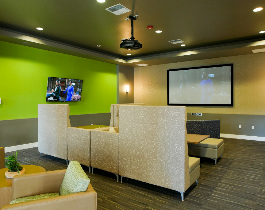 Modern lounge with green accent wall, wall-mounted TV, projector screen, and beige seating area