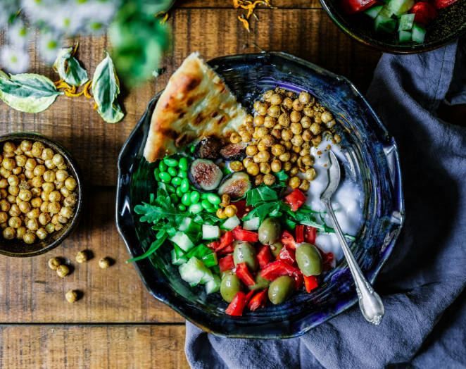 Colorful salad bowl with chickpeas, greens, tomatoes, olives, and a spoon on a wooden table