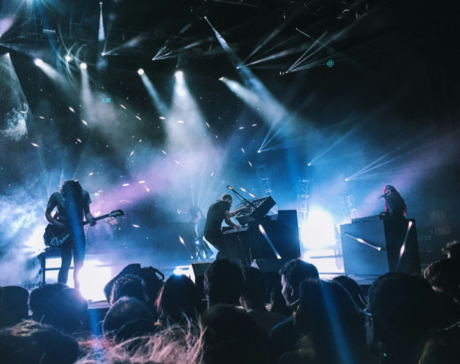 Rock band performing on a stage with blue and purple lights, silhouetted crowd in front