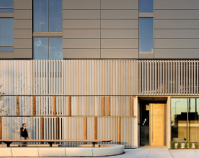 Modern building facade with vertical slats, glass entrance, and a person walking by on the left