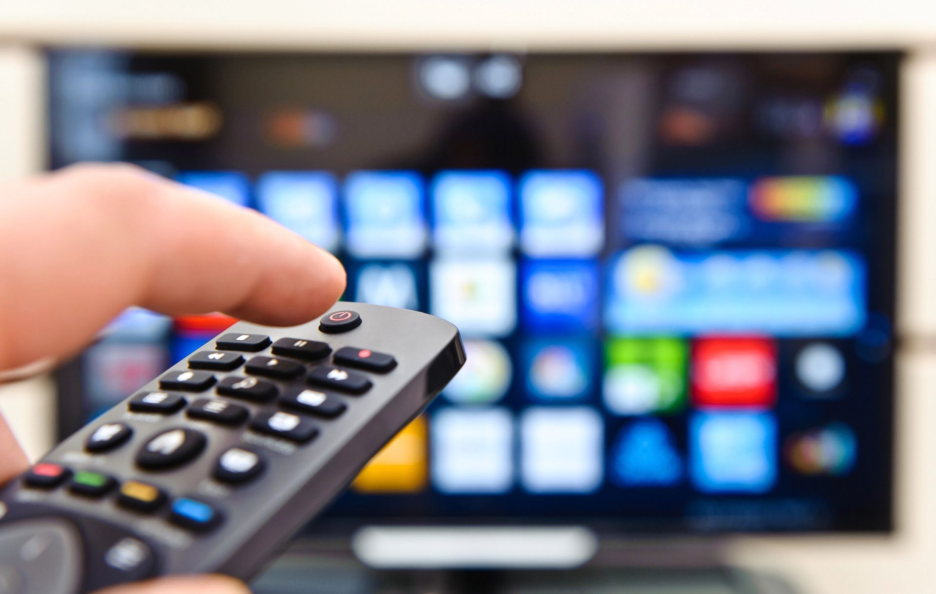 Una mano que sostiene un control remoto apunta a una pantalla de televisión borrosa con iconos de aplicaciones.