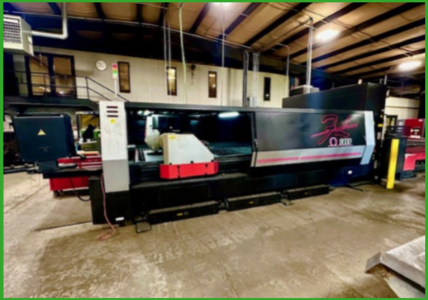 A large industrial laser cutting machine with black and red panels in a manufacturing facility.