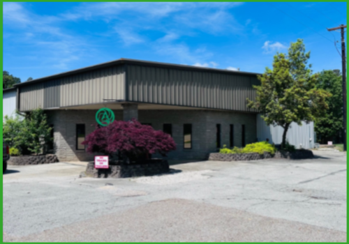 A single-story commercial building with tan metal siding and a dark brick facade under a bright blue sky.