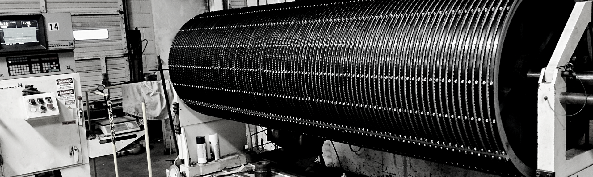 A large, cylindrical industrial machine with a patterned metal mesh surface in a workshop setting.