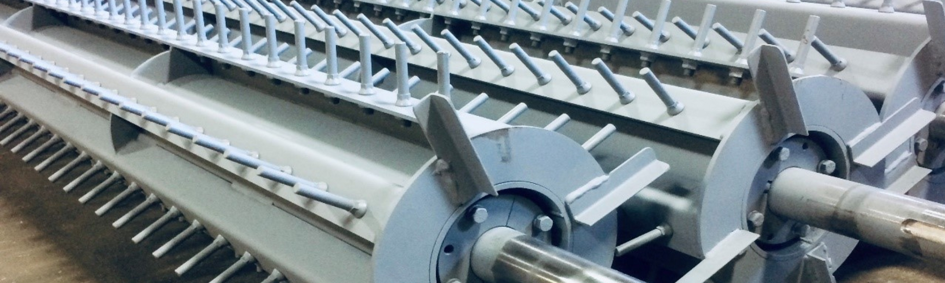 Two industrial rotating drums with metal paddles and shafts, painted in grey, positioned in a manufacturing facility.