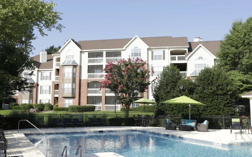 Apartment building with pool, trees, and green umbrellas on a sunny day.