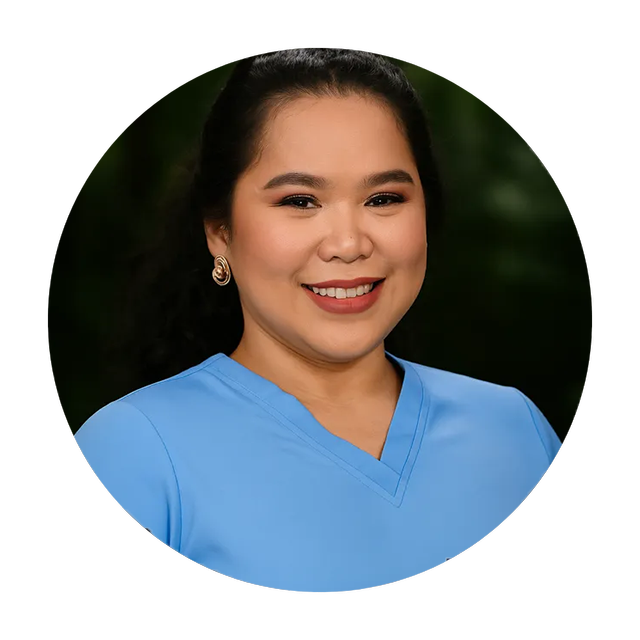 Woman in light blue top smiles, framed in a circle. Dark hair pulled back, gold earrings, dark background.