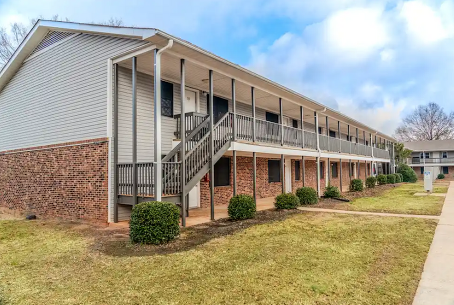 Two-story apartment building with brick and siding, featuring a walkway, stairs, and shrubs.