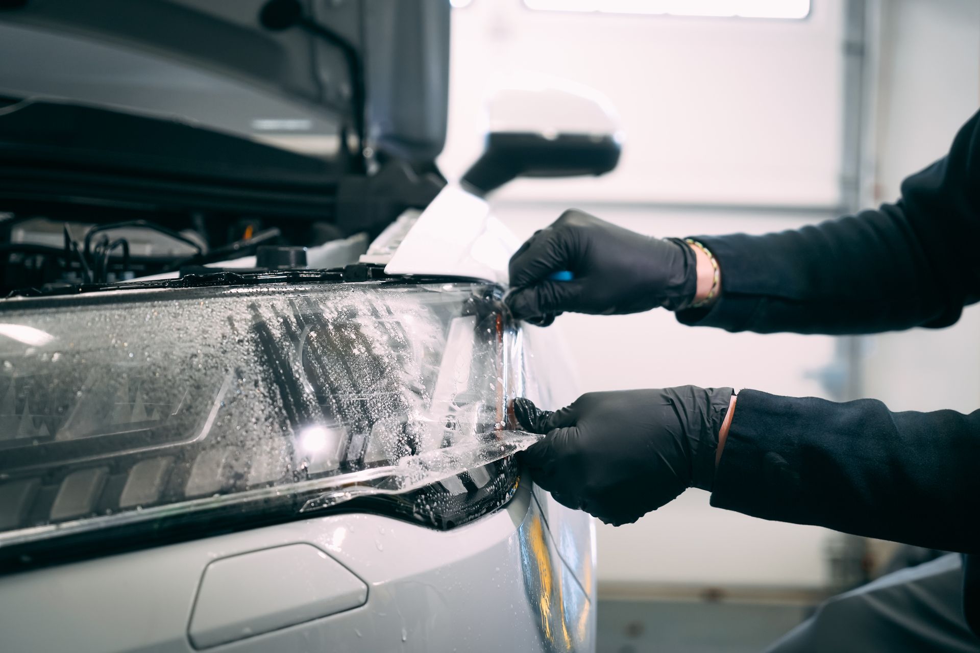 A man is applying a protective film to the headlight of a car.