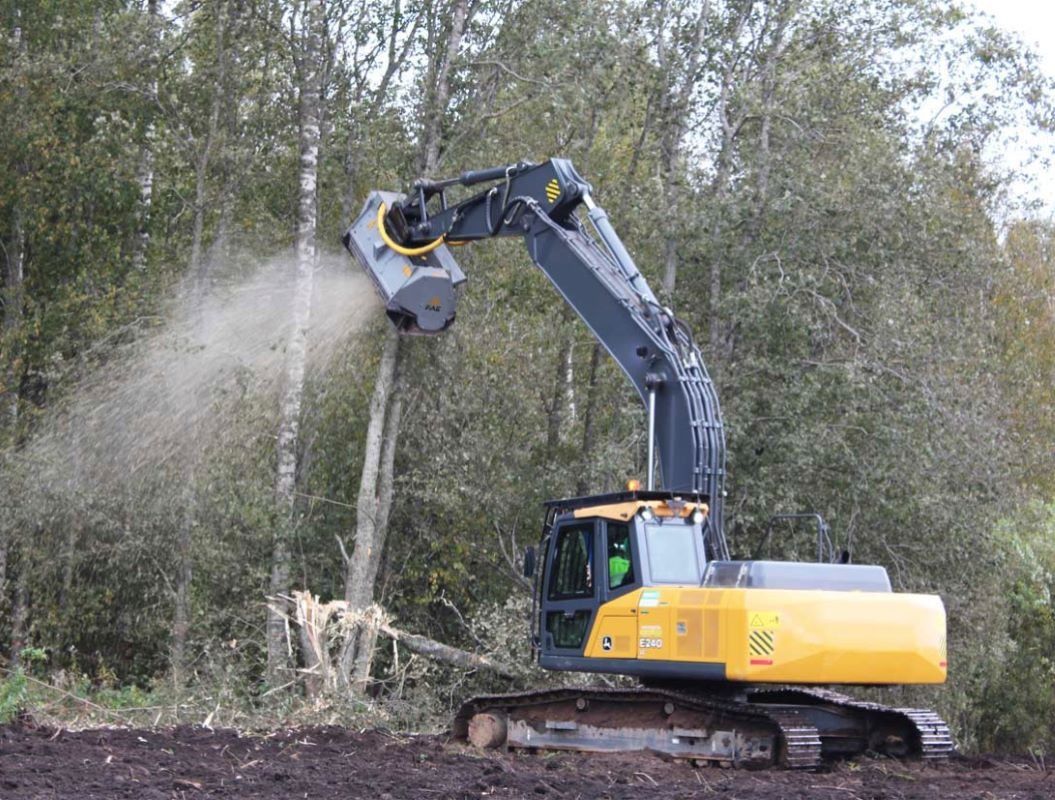 Yellow excavator mulching trees in a forest, creating wood chips.