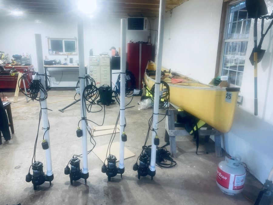 Four submersible pumps with attached PVC pipes inside a garage. A canoe and propane tank are also visible.