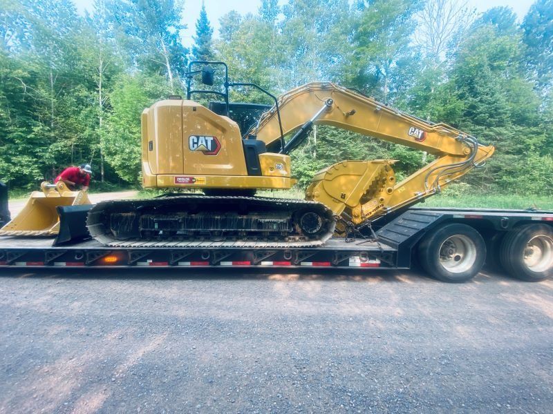 Yellow Caterpillar excavator on a flatbed trailer, ready for transport, trees in the background.