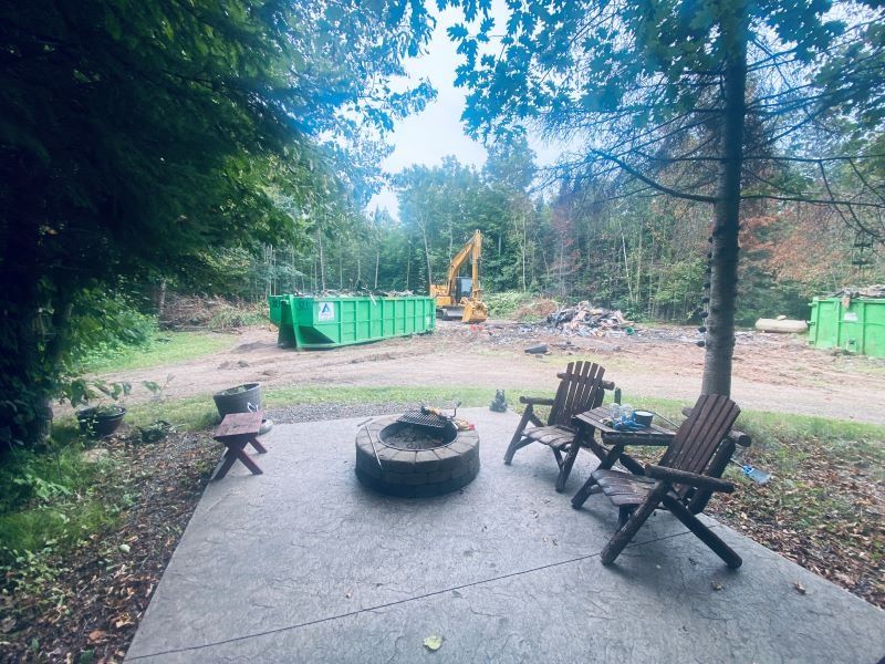 Patio with fire pit, chairs, construction in background with excavator, dumpsters, and cleared land.