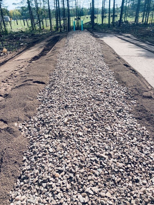 A gravel pathway bordered by dirt and concrete with trees in the background.