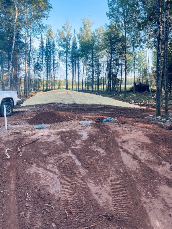 Dirt road leading to a leveled, grassy area in a wooded setting.