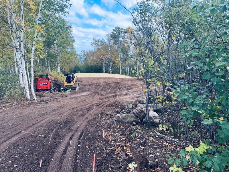 Construction site with two pieces of heavy machinery on a cleared dirt area surrounded by trees.