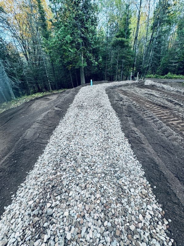 Gravel path winding through a construction site towards trees, with dark soil on either side.