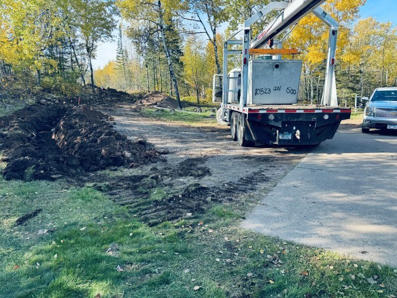 Truck unloading a concrete block near dirt pile. Trees with yellow leaves in background.