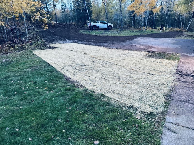 Lawn area covered with straw, next to driveway. A truck is parked in the background.