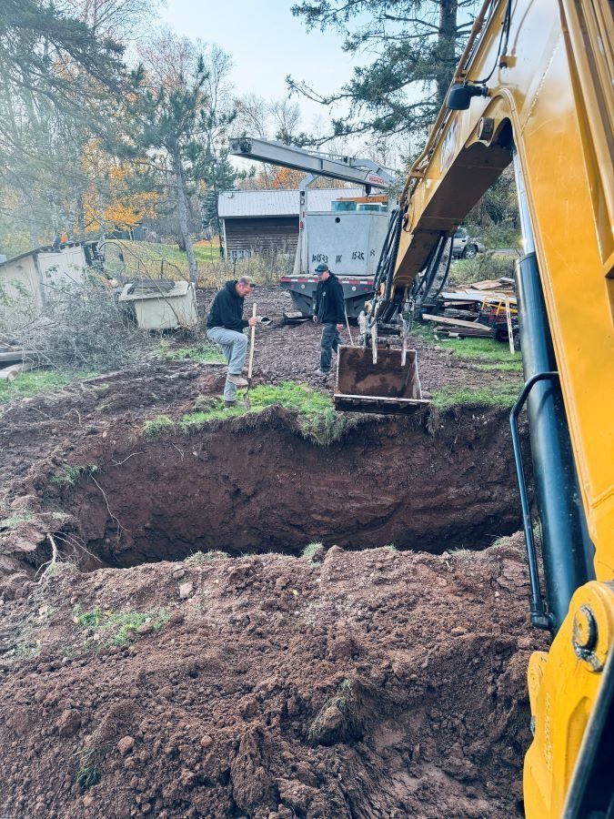 Two men dig in a hole with an excavator in a backyard.