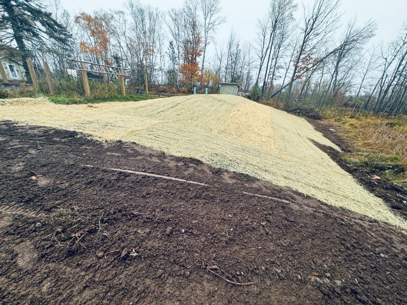 A hillside covered in yellow straw and newly turned dark soil, trees in the background.