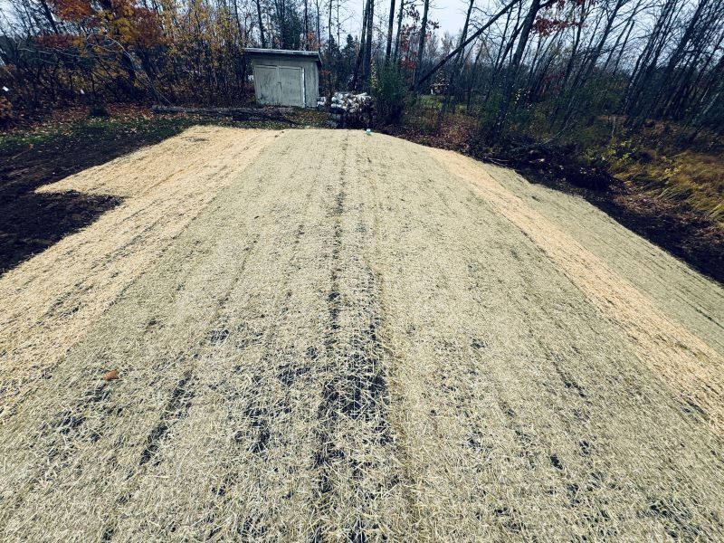 A freshly seeded slope covered in straw, leading to a small concrete structure in a wooded area.