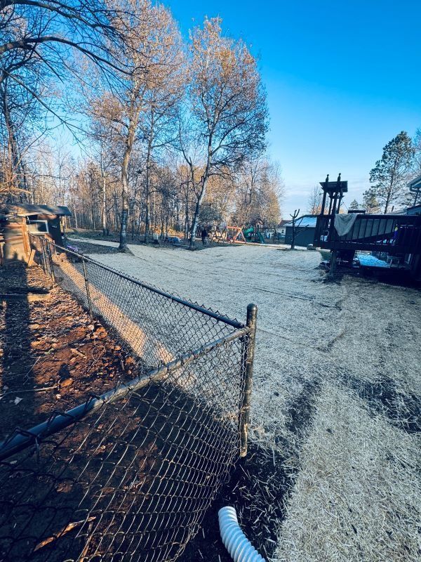 A gravel yard next to a fence with trees and blue sky in the background.