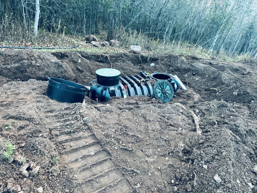A septic system installation in progress outdoors. Exposed pipes, tanks, and earth.