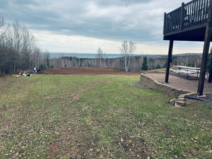 Grassy yard with partial view of a lake and cloudy sky. A deck is on the right side.
