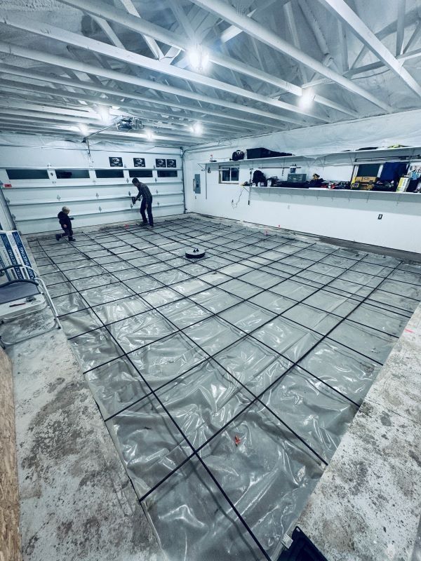 Workers preparing a garage floor for concrete, with rebar grid over plastic sheeting.
