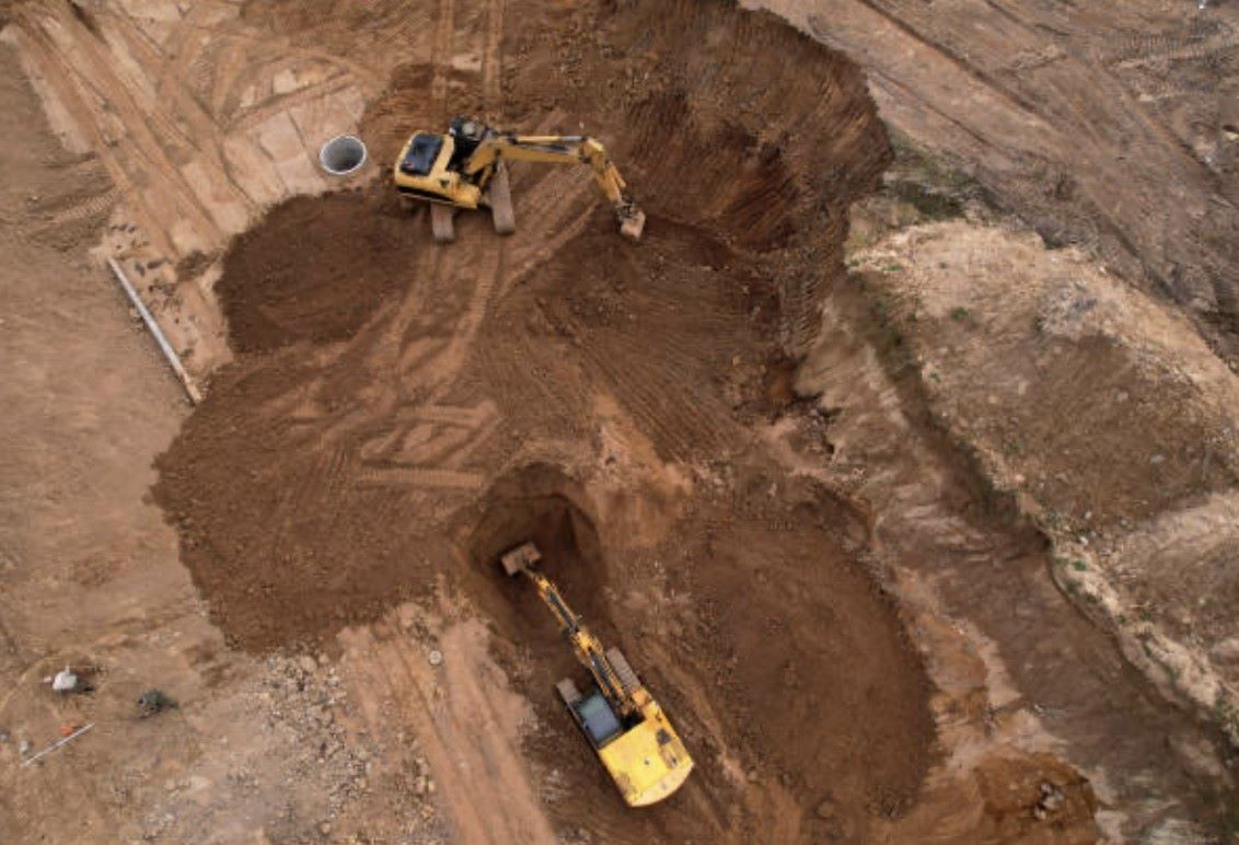 Two yellow excavators digging in brown soil at a construction site.