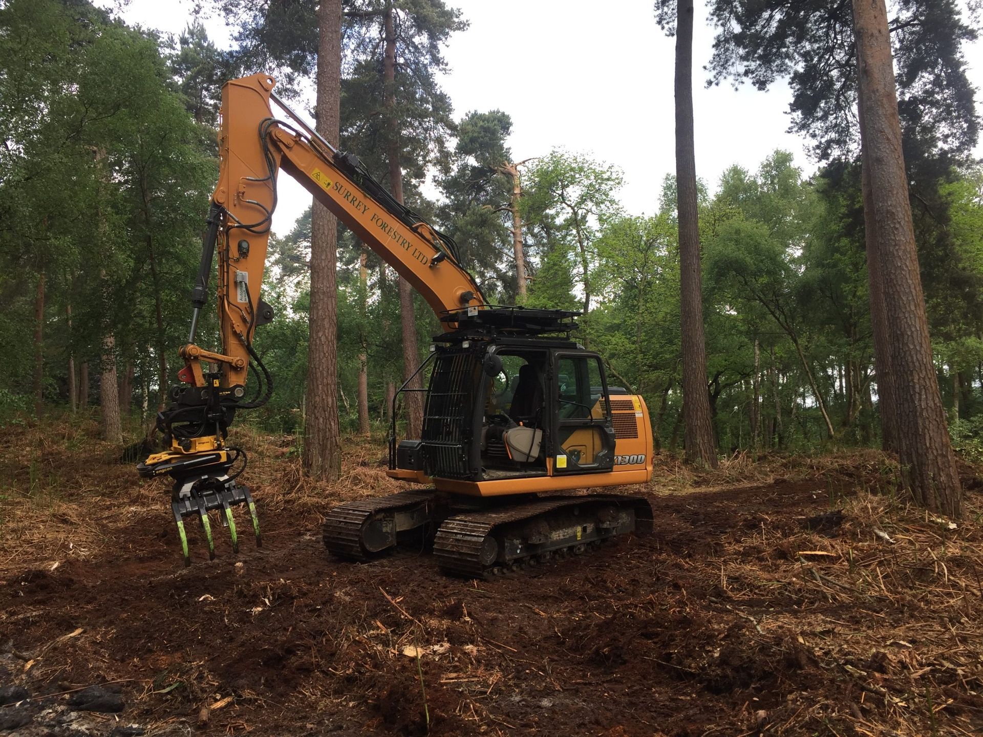 Yellow excavator with claw attachment clearing debris in a forest.