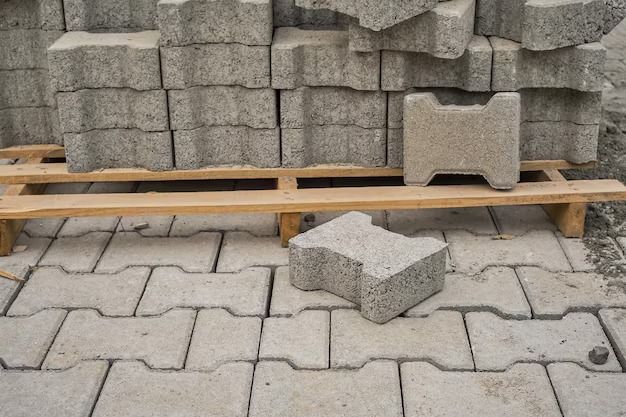 Gray interlocking paving stones stacked on a pallet, with one on the ground.